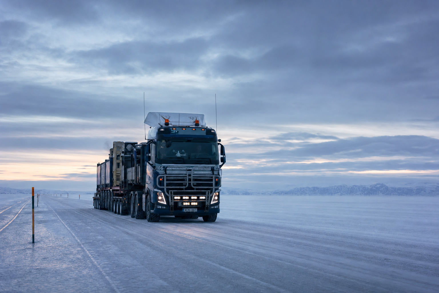 A heavy transport truck driving across a vast frozen lake under a moody, Arctic twilight sky.